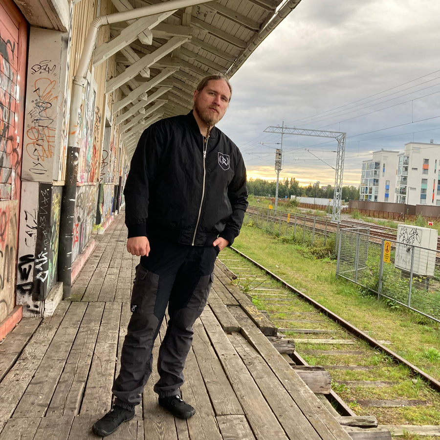 Rurik Fightgear-lentäjänpusakka.
Rurik FG "R" -logo rintapielessä sekä riimulogo selässä monivärisesti brodeerattuna. Kuvassa pilottitakki Mikan päällä junan laiturilla. ptcumbat.com