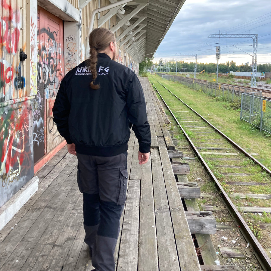 Rurik Fightgear-lentäjänpusakka.
Rurik FG "R" -logo rintapielessä sekä riimulogo selässä monivärisesti brodeerattuna. Kuvassa pilottitakki  Mikan päällä takaa kuvattuna. ptcumbat.com